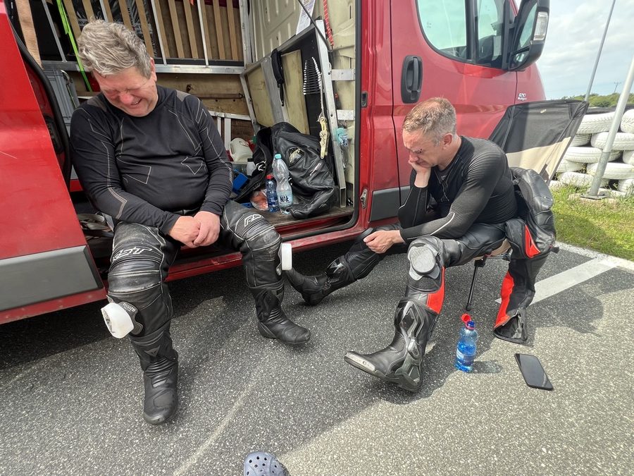 Andrzej and Rafał next to the van in the paddock, wearing motorcycle race suits